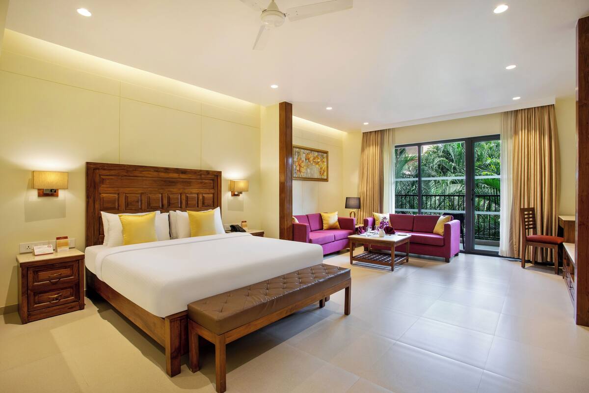 A hotel room with a large bed, a bench, a sofa, and a dining area.