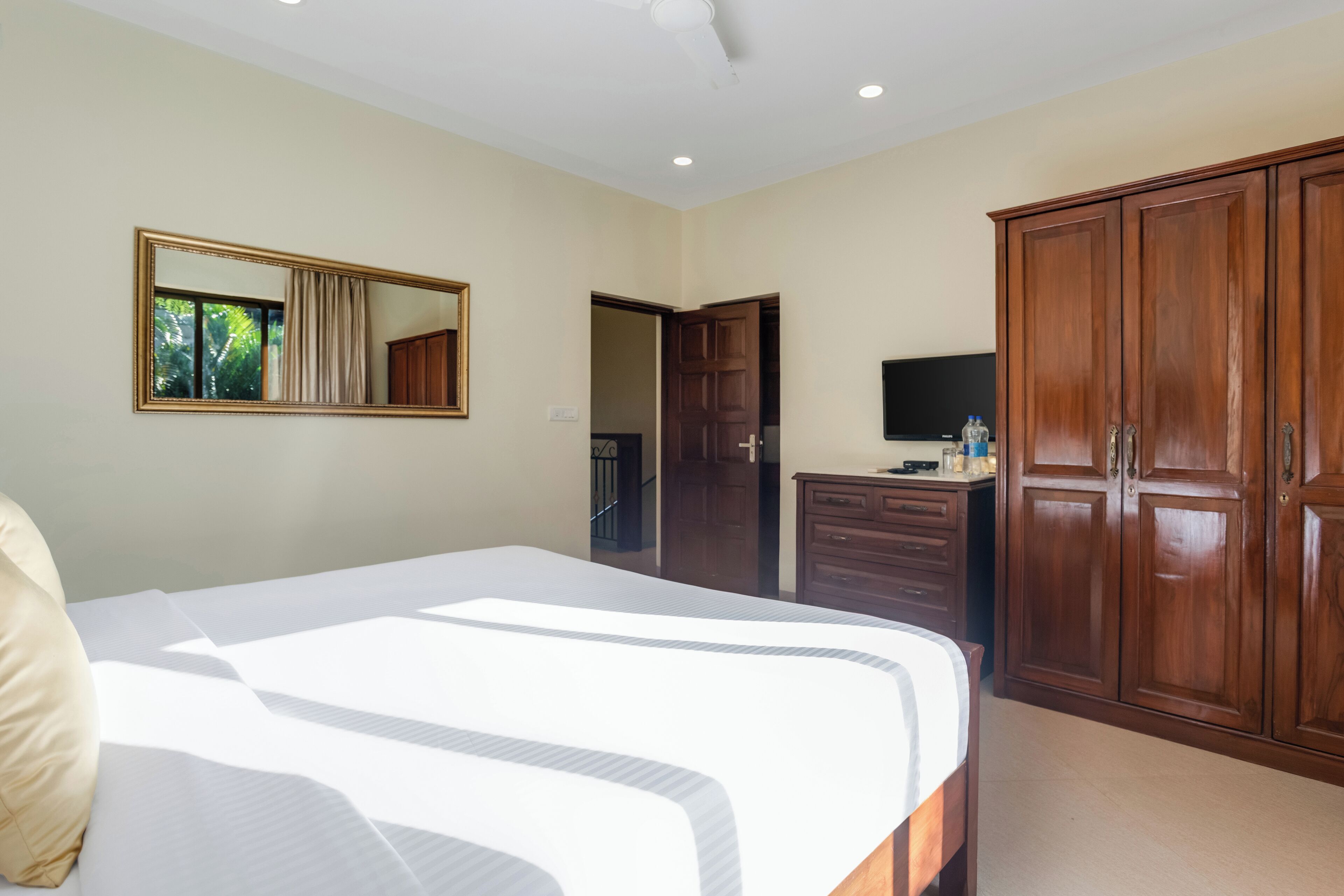 A bedroom with a large bed, a wardrobe, a television, and a mirror.