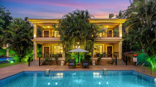 Un hotel de dos pisos con piscina, rodeado de exuberante follaje y palmeras.