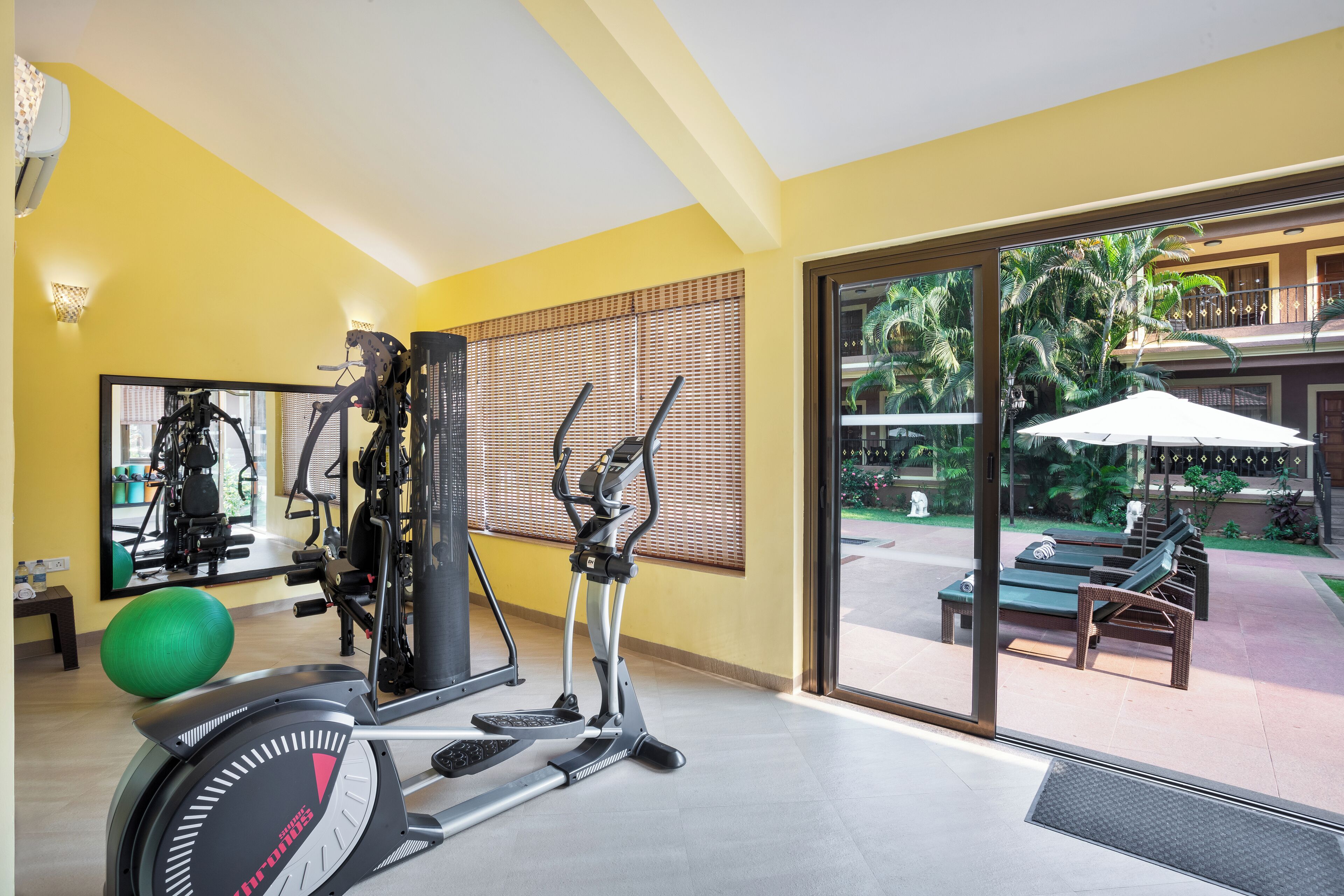 A gym with exercise equipment, a large mirror, and a view of a pool and outdoor seating area.