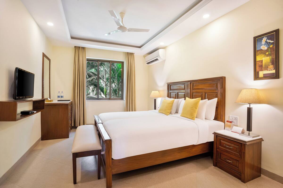 A hotel room with a large bed, bedside tables, a desk, a television, and a window with curtains.