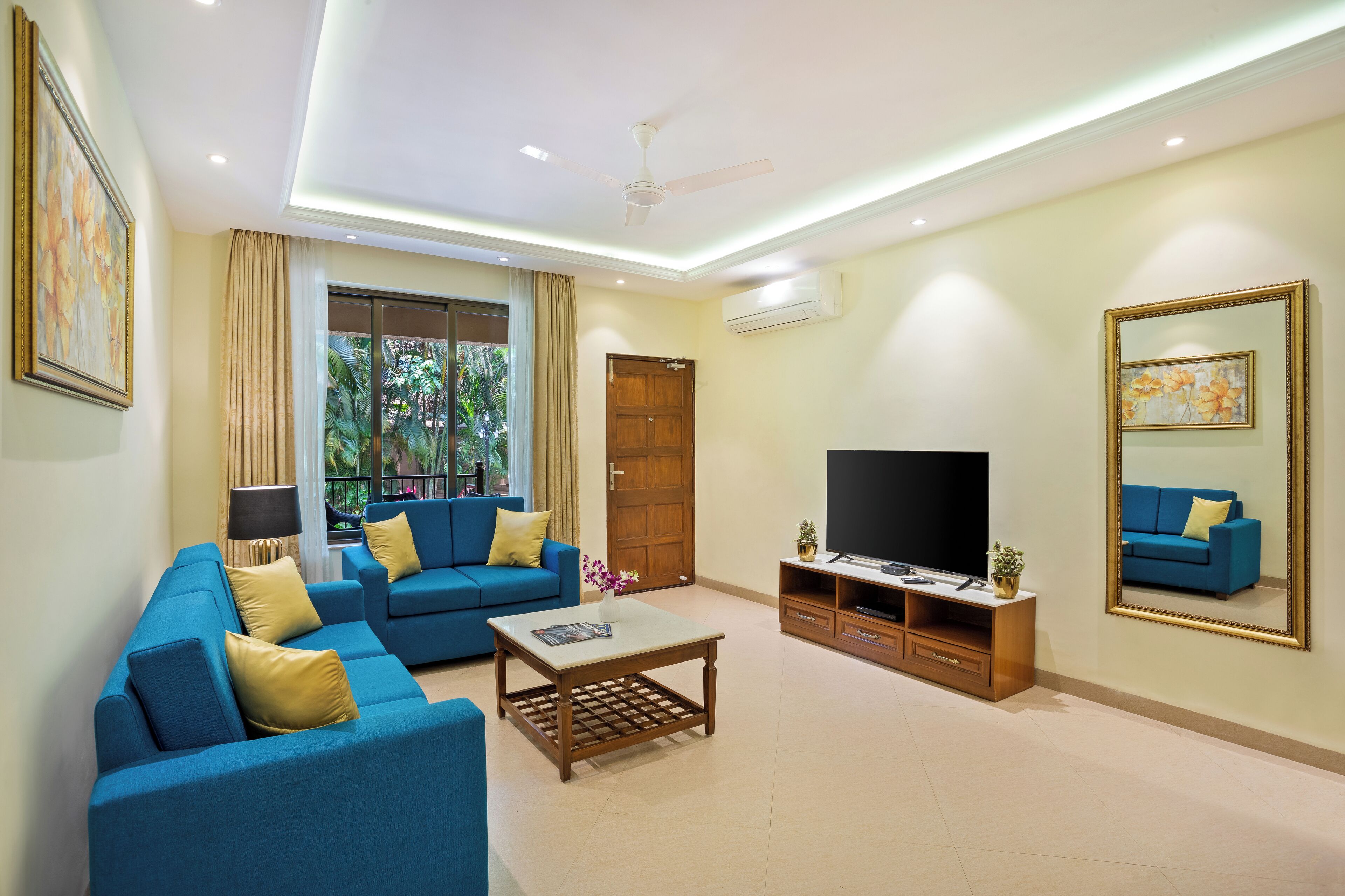 A modern living room with a blue sofa set, a coffee table, a flat-screen TV, and a large mirror.