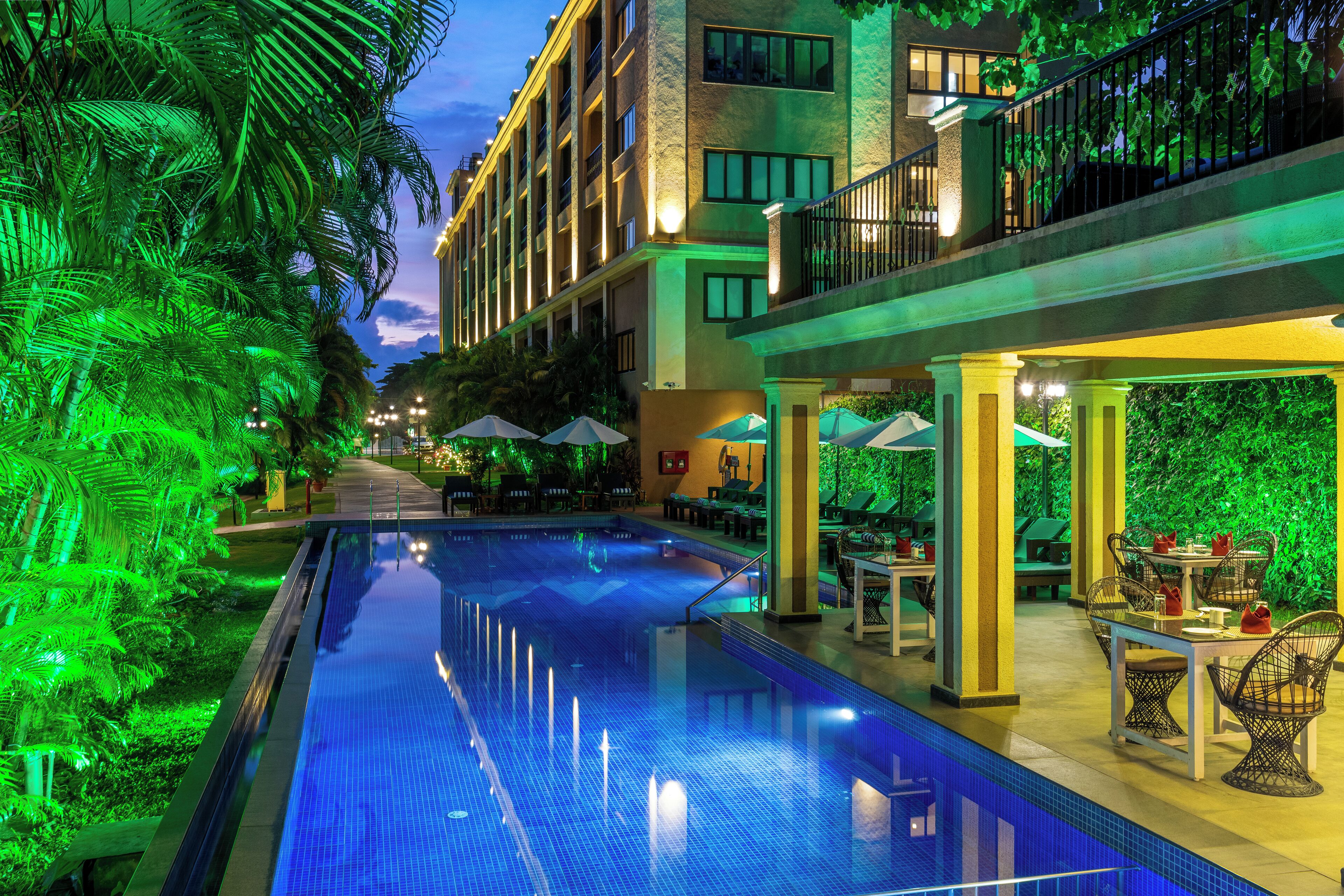 Ein Swimmingpool mit einer umlaufenden Terrassenanlage, einschließlich Tischen und Stühlen, und ein Gebäude mit Balkonen.