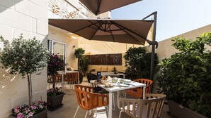 Un espace extérieur aménagé en terrasse, avec une table et des chaises, entouré de plantes en pot et doté d’un grand parasol pour créer de l’ombre.