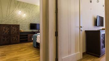 A hotel room with a wooden floor, a bed, a TV, a wardrobe, and a wall with a tree mural.