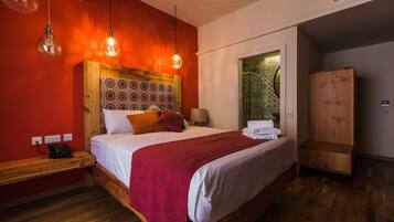 Un dormitorio con cabecera de madera, cama con ropa de cama blanca y manta roja, mesita de noche con teléfono y armario.