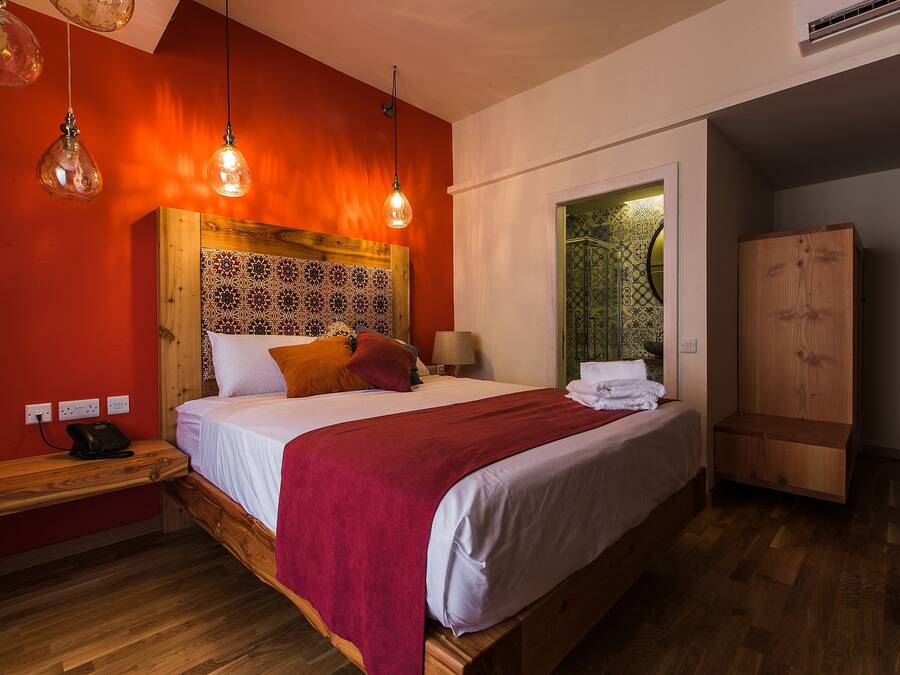 Un dormitorio con cabecera de madera, cama con ropa de cama blanca y manta roja, mesita de noche con teléfono y armario.