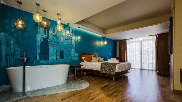Une chambre spacieuse avec un grand lit, une baignoire et une fresque murale.