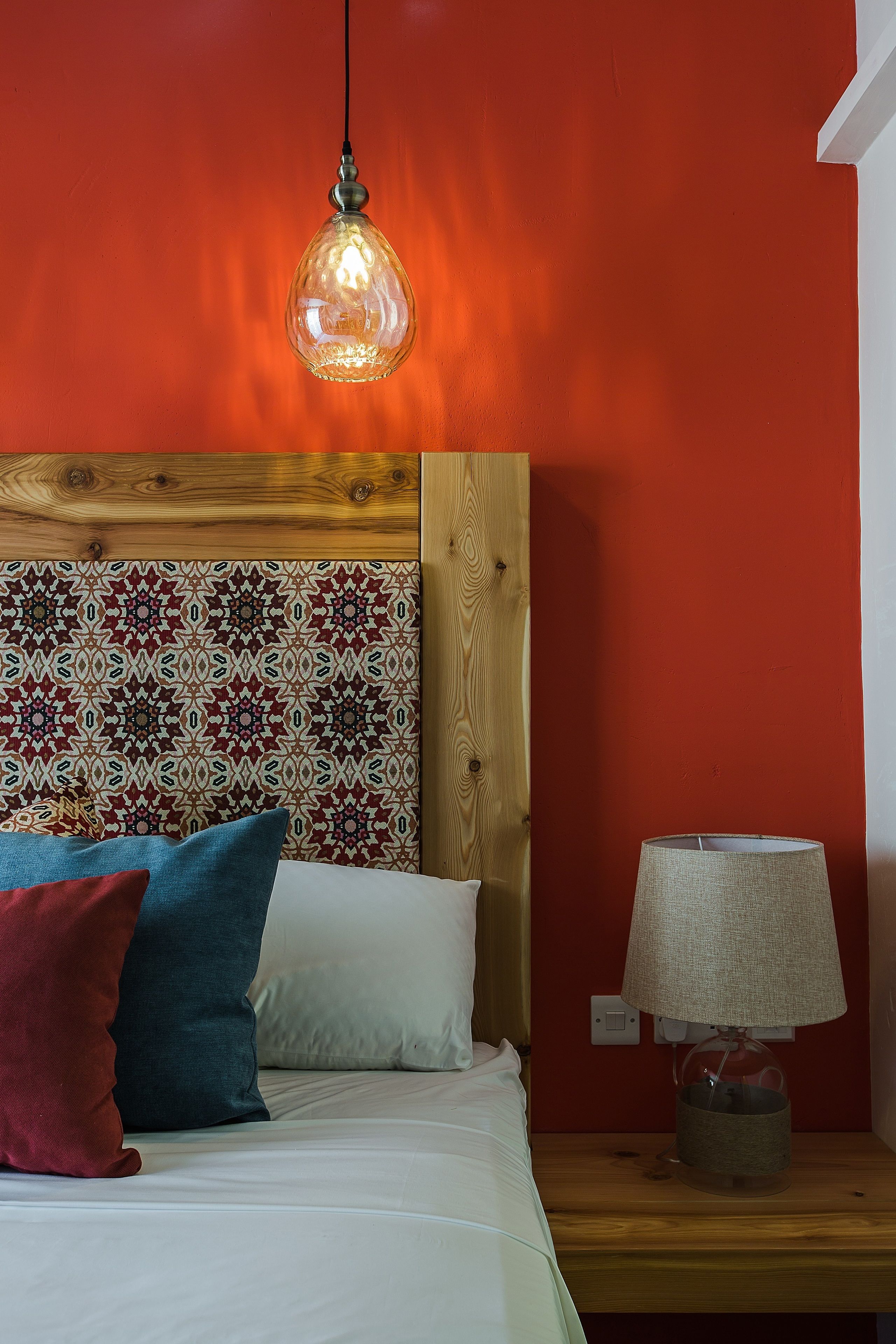 A bedroom with a wooden headboard, a bed with white and red pillows, a hanging light fixture, and a nightstand with a lamp.