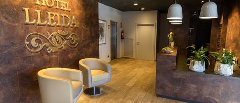 A hotel reception area with a modern design, featuring a reception desk, two seating areas, and a wall-mounted sign that reads "HOTEL LLEIDA".