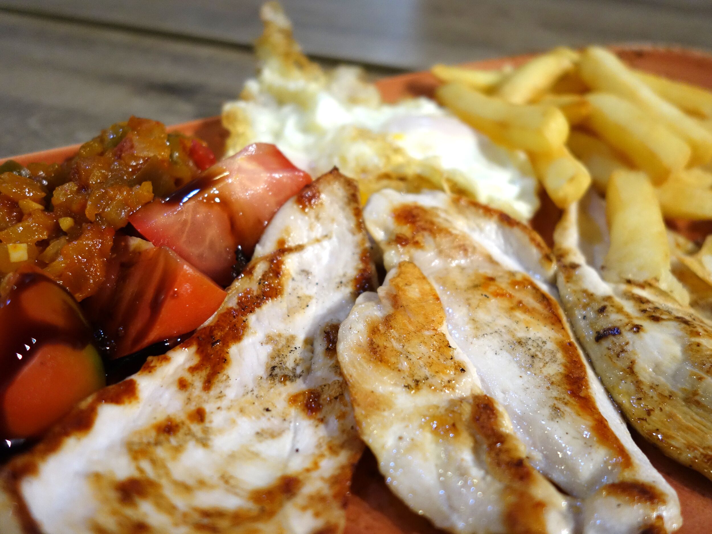 Des filets de poisson grillés, des frites et une sauce à base de tomates, le tout servi sur une assiette.