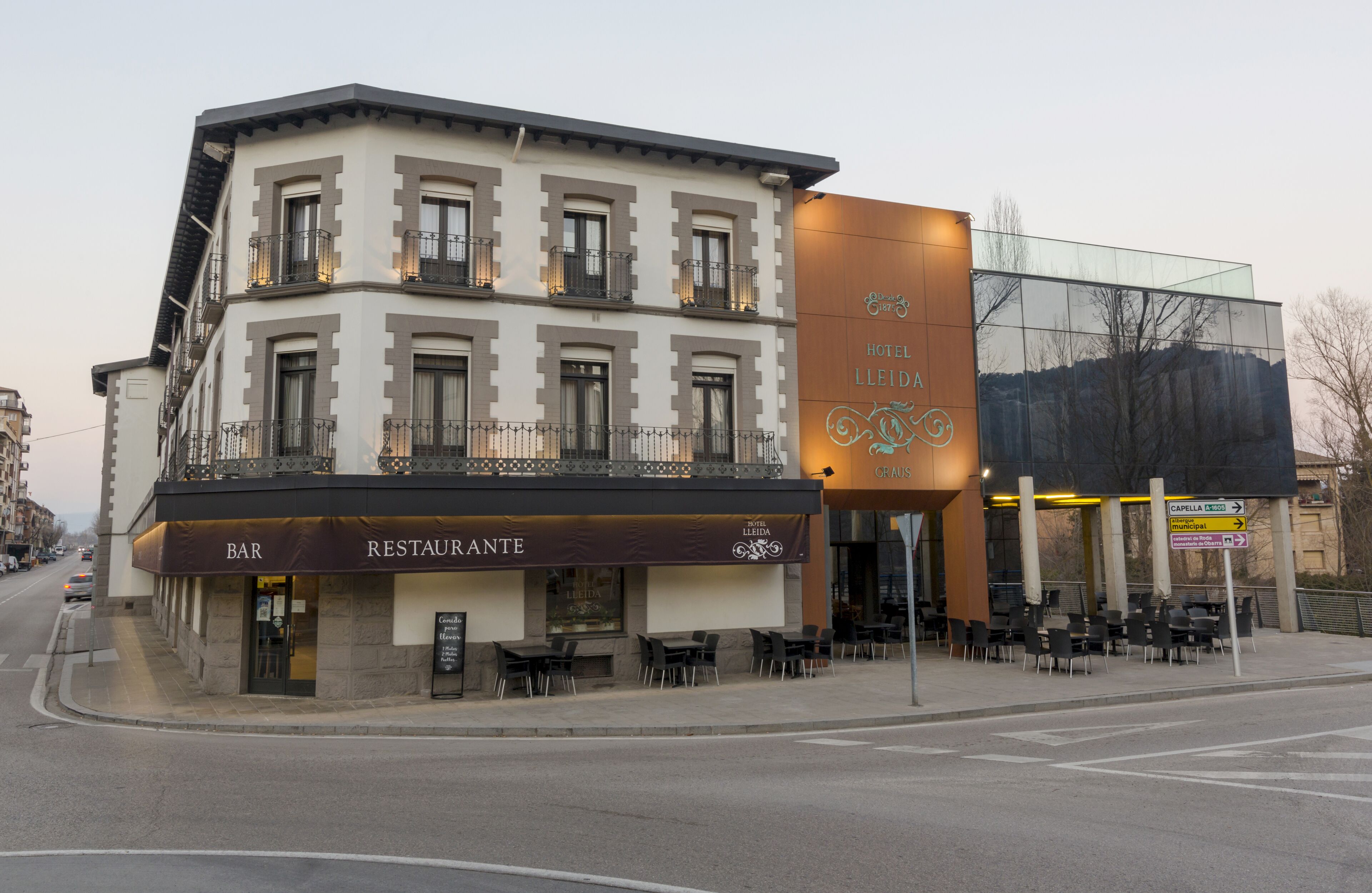 A hotel with a bar and restaurant on the ground floor, outdoor seating, and a modern glass building to the right.