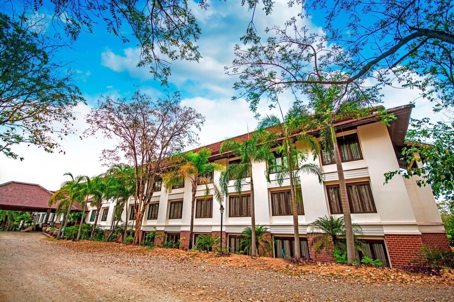 A multi-story hotel with a white facade, multiple balconies, and surrounding palm trees.