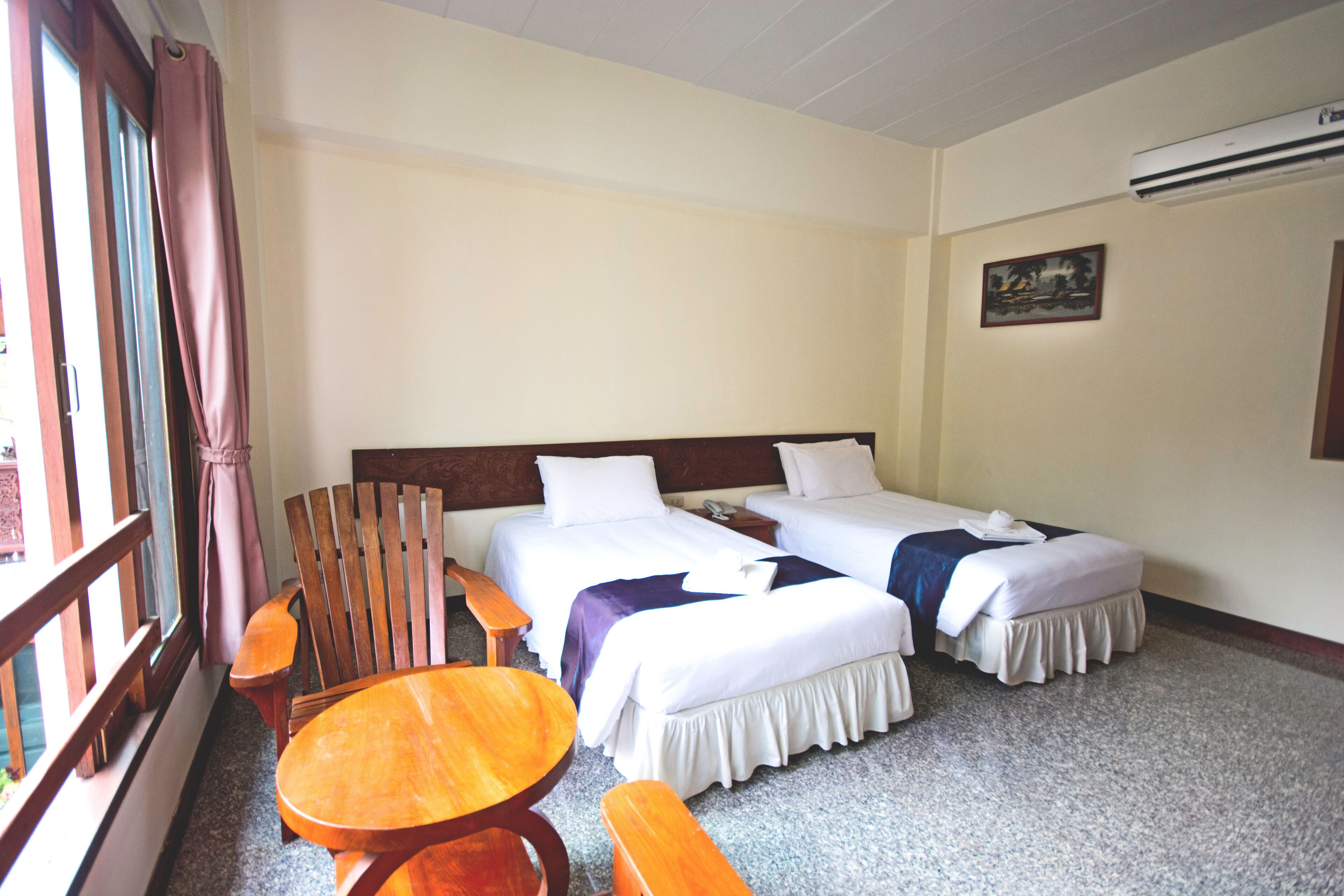 A hotel room with two beds, a wooden table, and a bench.
