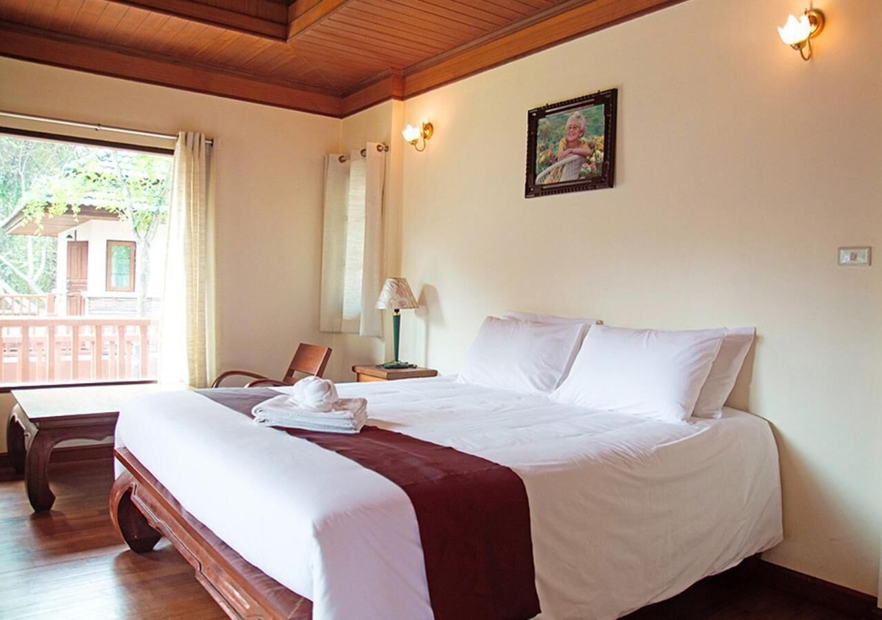 Een hotelkamer met een groot bed, een houten bureau, een stoel, een lamp en een schilderij aan de muur.