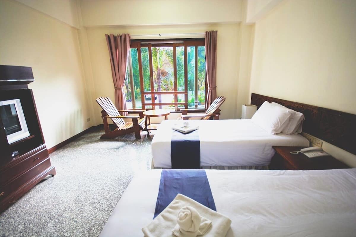 A hotel room with two beds, a TV, a desk with a chair, and a window with curtains.