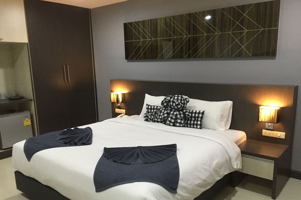 A modern hotel room with a large bed, dark wooden wardrobe, bedside lamps, and a geometric wall decoration.