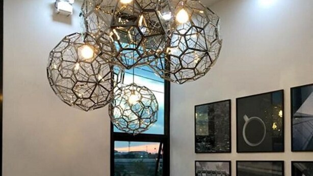 Un interior moderno con lámparas colgantes geométricas, un amplio ventanal con vistas y una serie de fotografías enmarcadas en la pared.