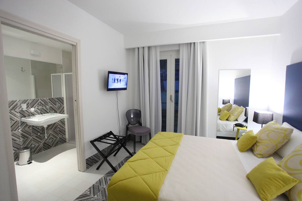 A modern hotel room with a bed, a television, a bathroom with a sink, and a chair.