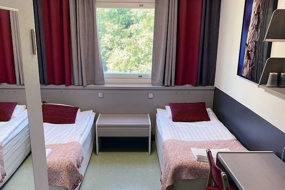 A hotel room with two beds, a desk, and a window with curtains.