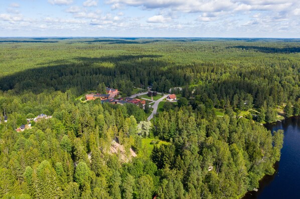 An aerial view of a forested area with several buildings, including a red-roofed structure and a house with a white fence. - Hotel Nuuksio - Conferences and events (Kirkkonummi)