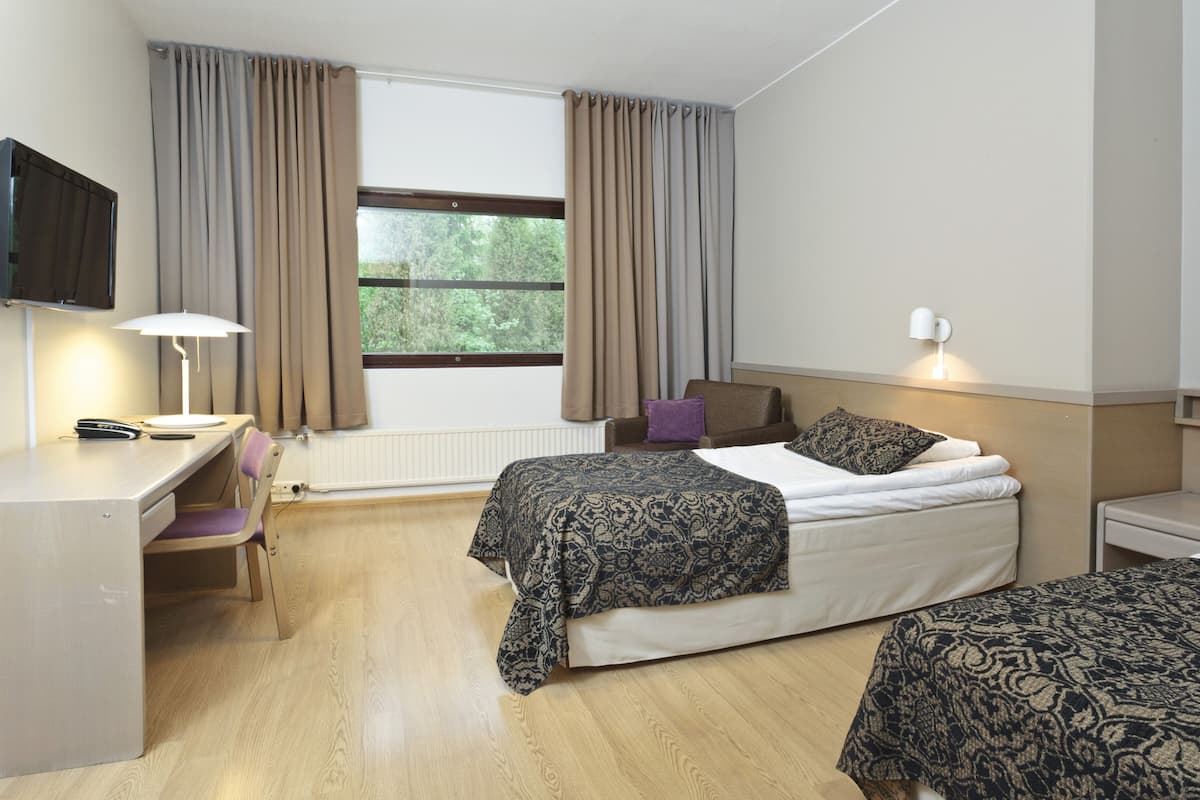 A hotel room with a bed, a desk, a chair, a TV, and a window with curtains.