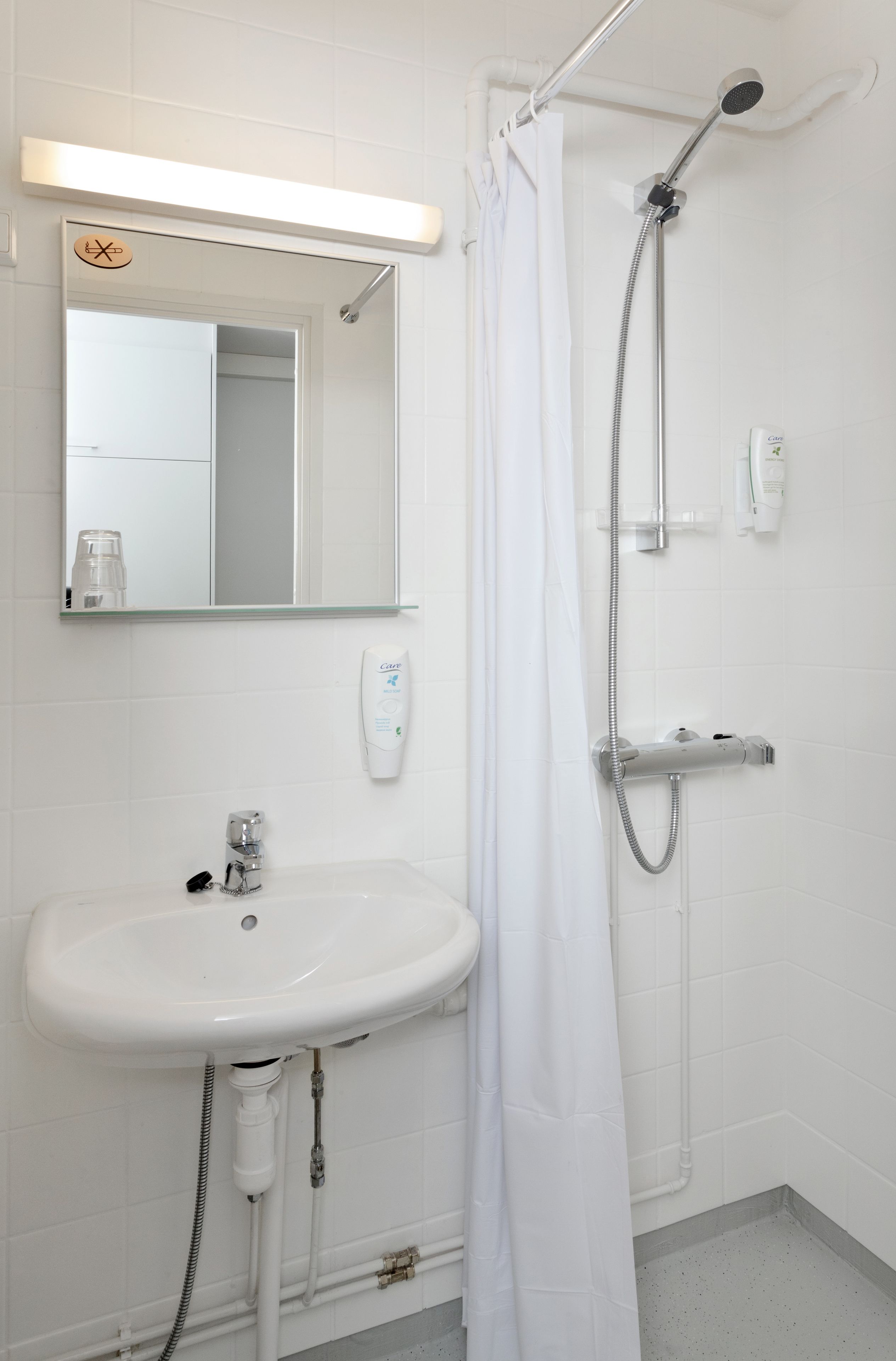 A bathroom with a white sink, a mirror, a shower with a handheld showerhead, and a white curtain.