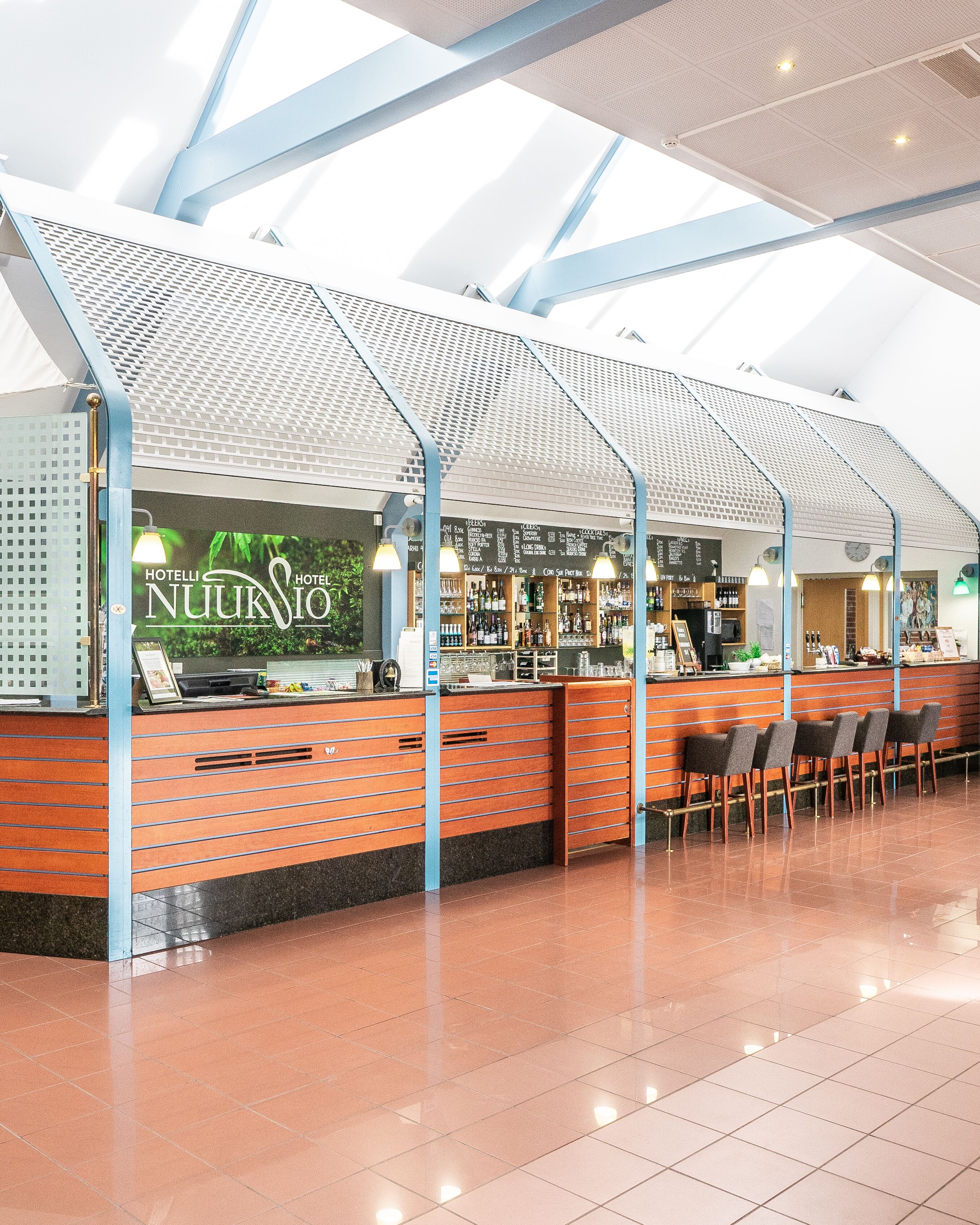 Un bar d’hôtel au design moderne, doté d’un comptoir avec un menu, de tabourets de bar et d’un plafond haut agrémenté de lucarnes.
