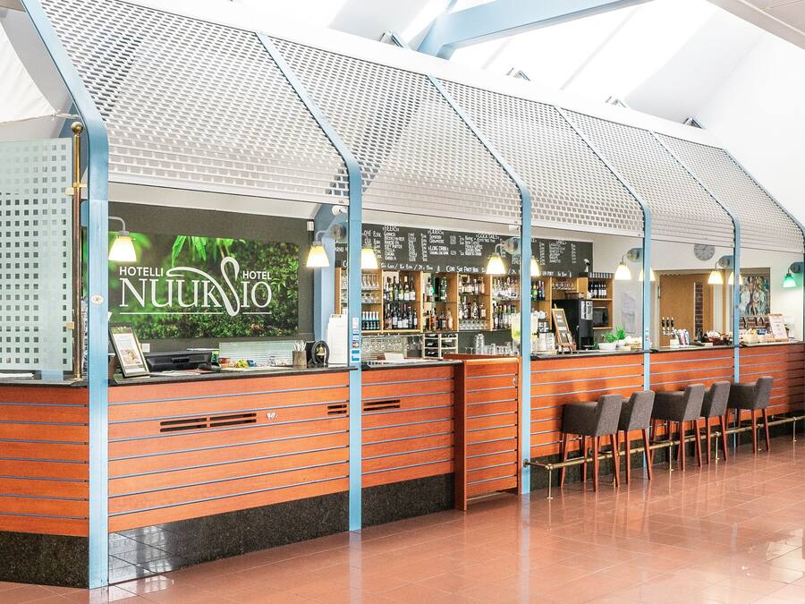 Un bar d’hôtel au design moderne, doté d’un comptoir avec un menu, de tabourets de bar et d’un plafond haut agrémenté de lucarnes.