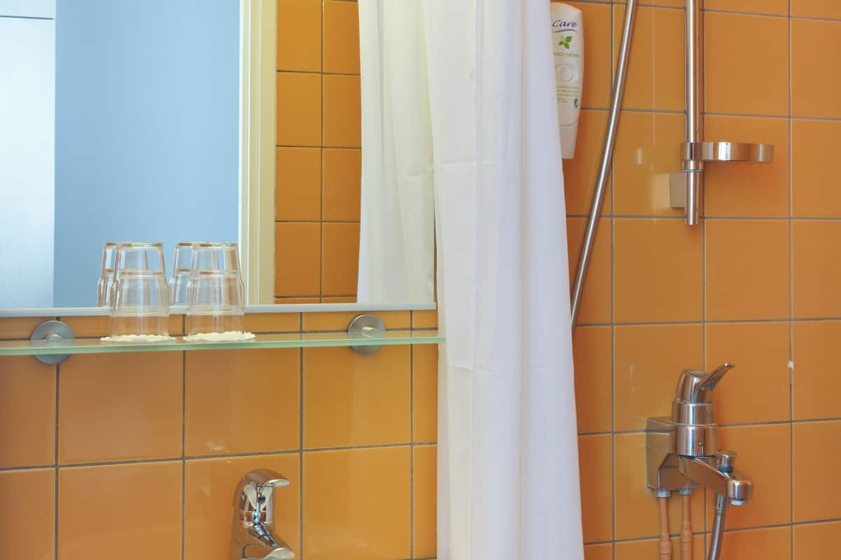 A bathroom with a sink, mirror, shower, and orange tiles.