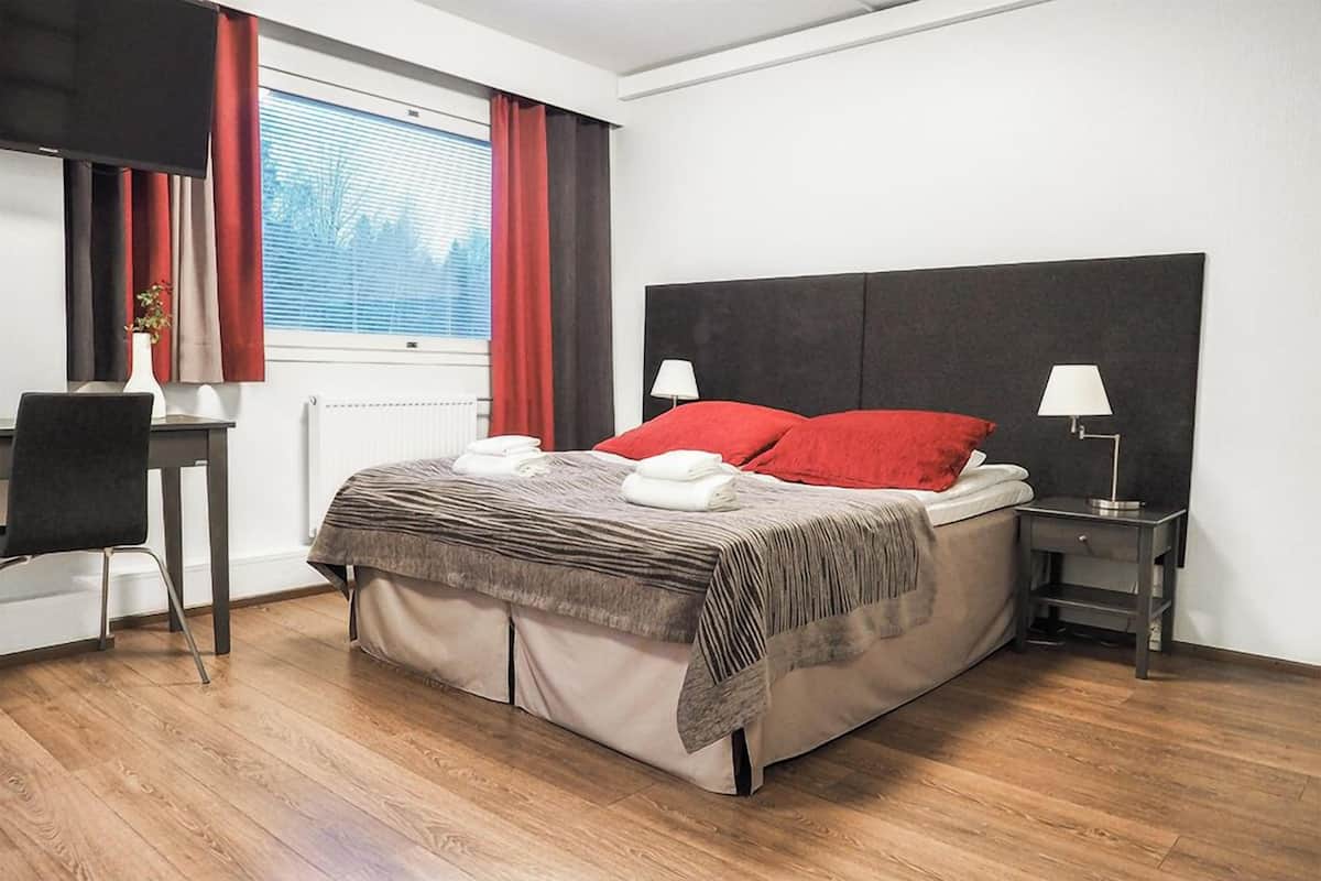 A modern bedroom with a large bed, two bedside tables with lamps, a desk with a chair, and a window with curtains.