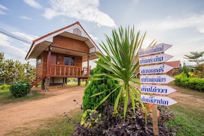 A wooden house with a balcony, surrounded by greenery and a signpost with multiple directional arrows.