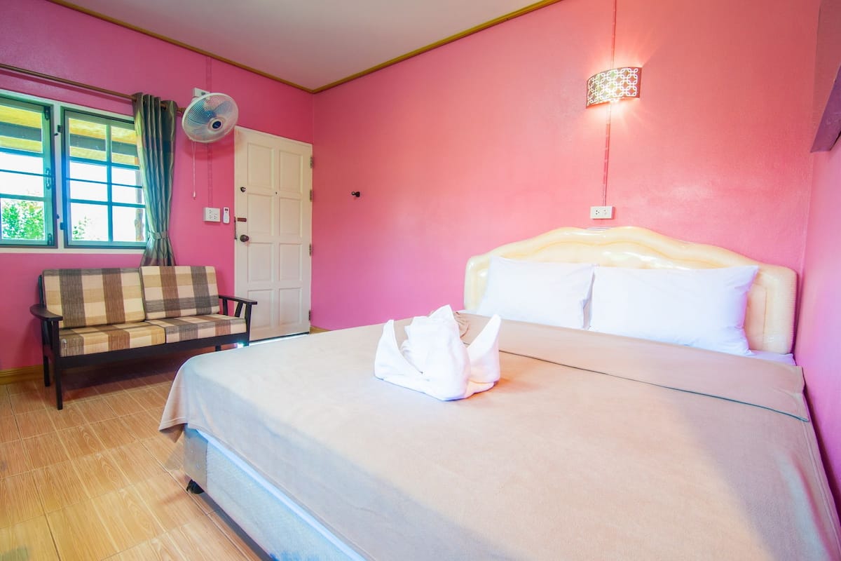 A bedroom with a bed, a sofa, a window with curtains, and a wall-mounted fan.