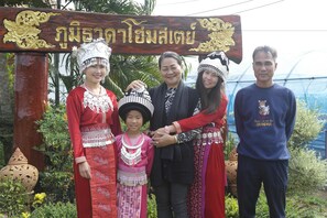 A group of people in traditional attire standing in front of a wooden sign with Thai script.