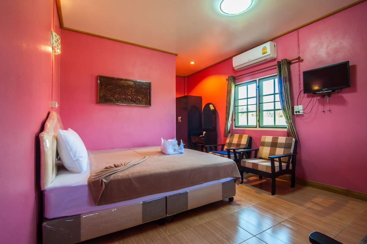 A hotel room with a bed, two chairs, a TV, and an air conditioning unit.