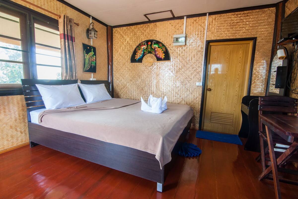 A neatly made bed with a beige blanket and white pillows, a wooden door, and a wall with a decorative fan.