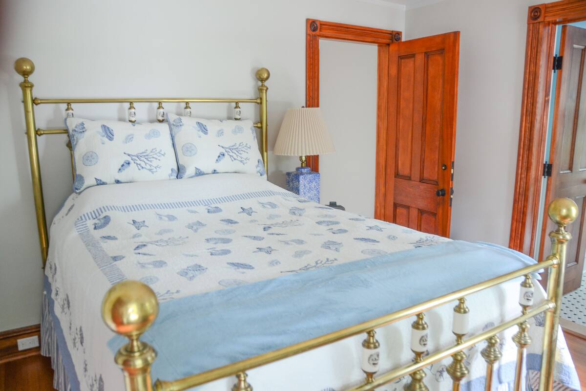 A bed with a patterned bedspread, a bedside lamp, and a wooden door in the background.
