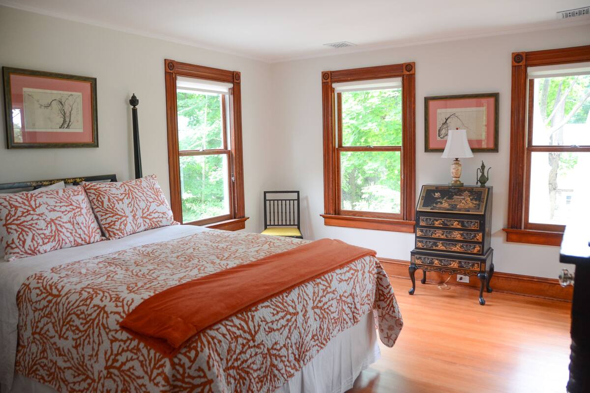 A bedroom with a large bed, two windows, a nightstand, and a dresser.