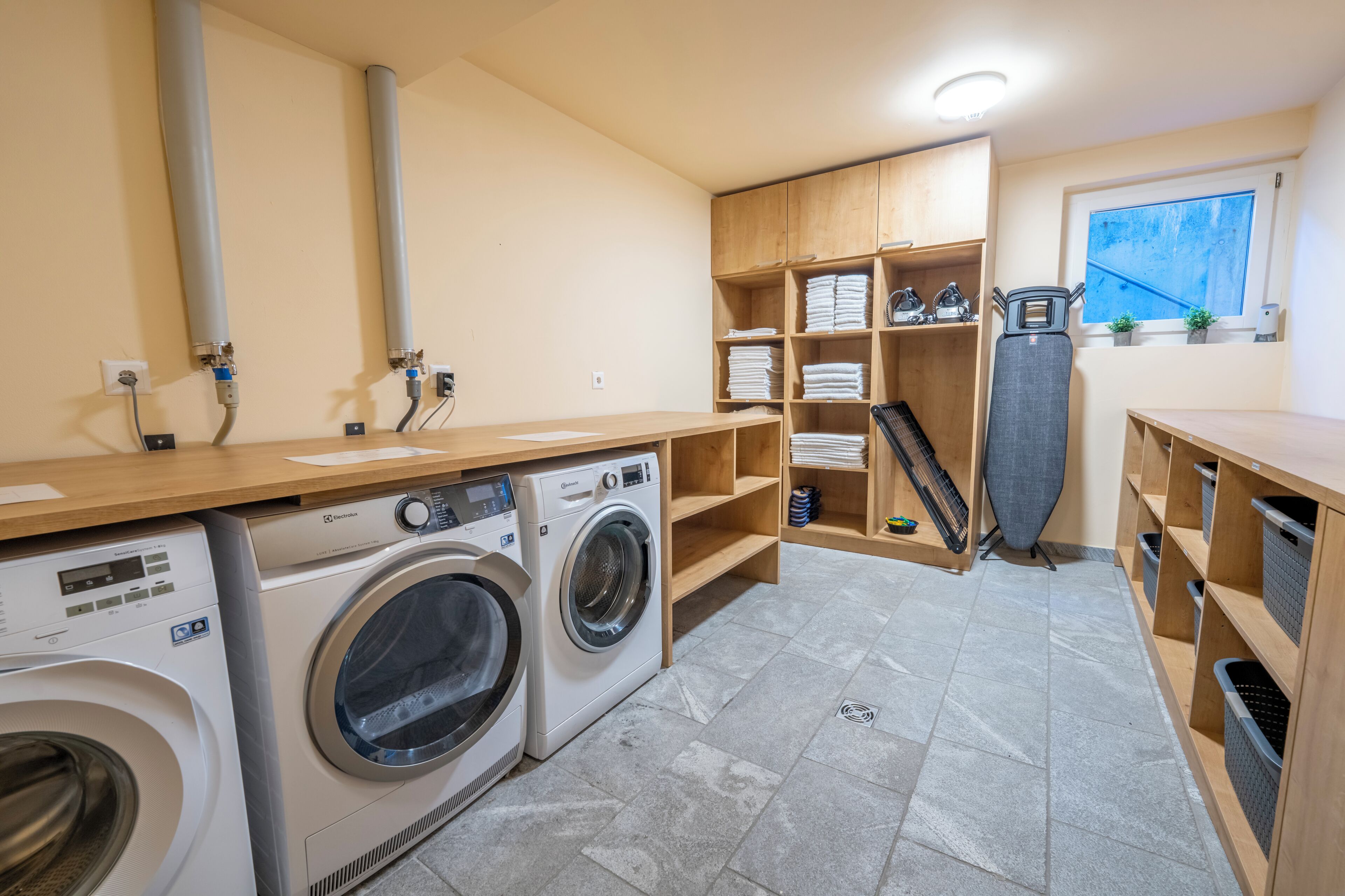 A laundry room with two washing machines, wooden shelving with folded towels, and a drying rack.