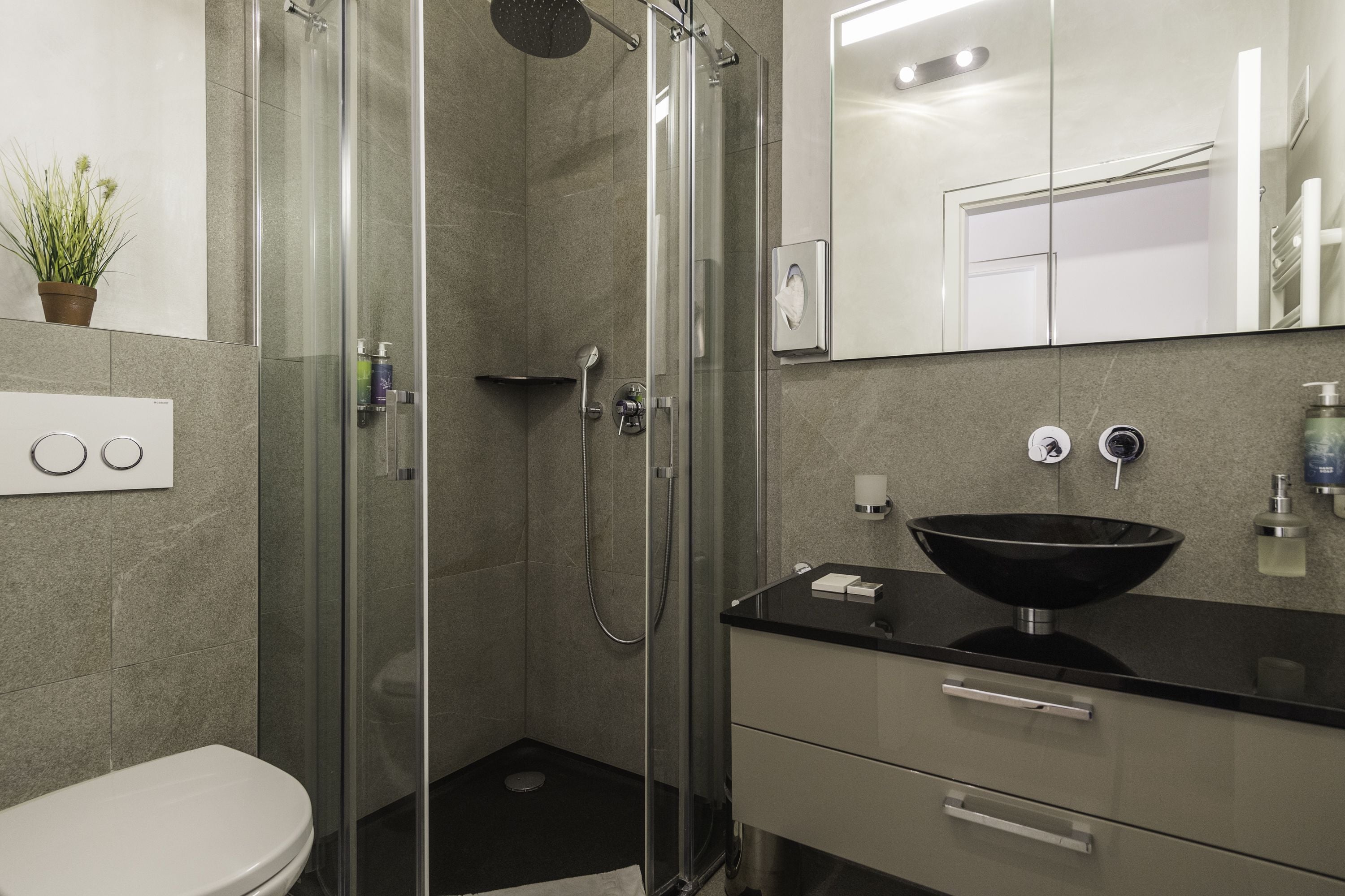 A modern bathroom with a glass-enclosed shower, a black sink, and a white toilet.
