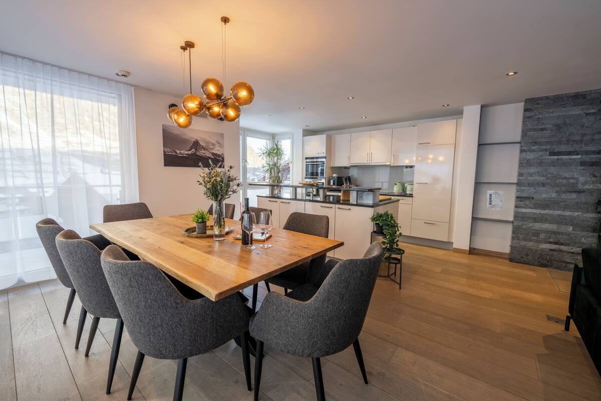 Eine moderne Küche mit weißen Schränken, einem Holztisch und grauen Stühlen.