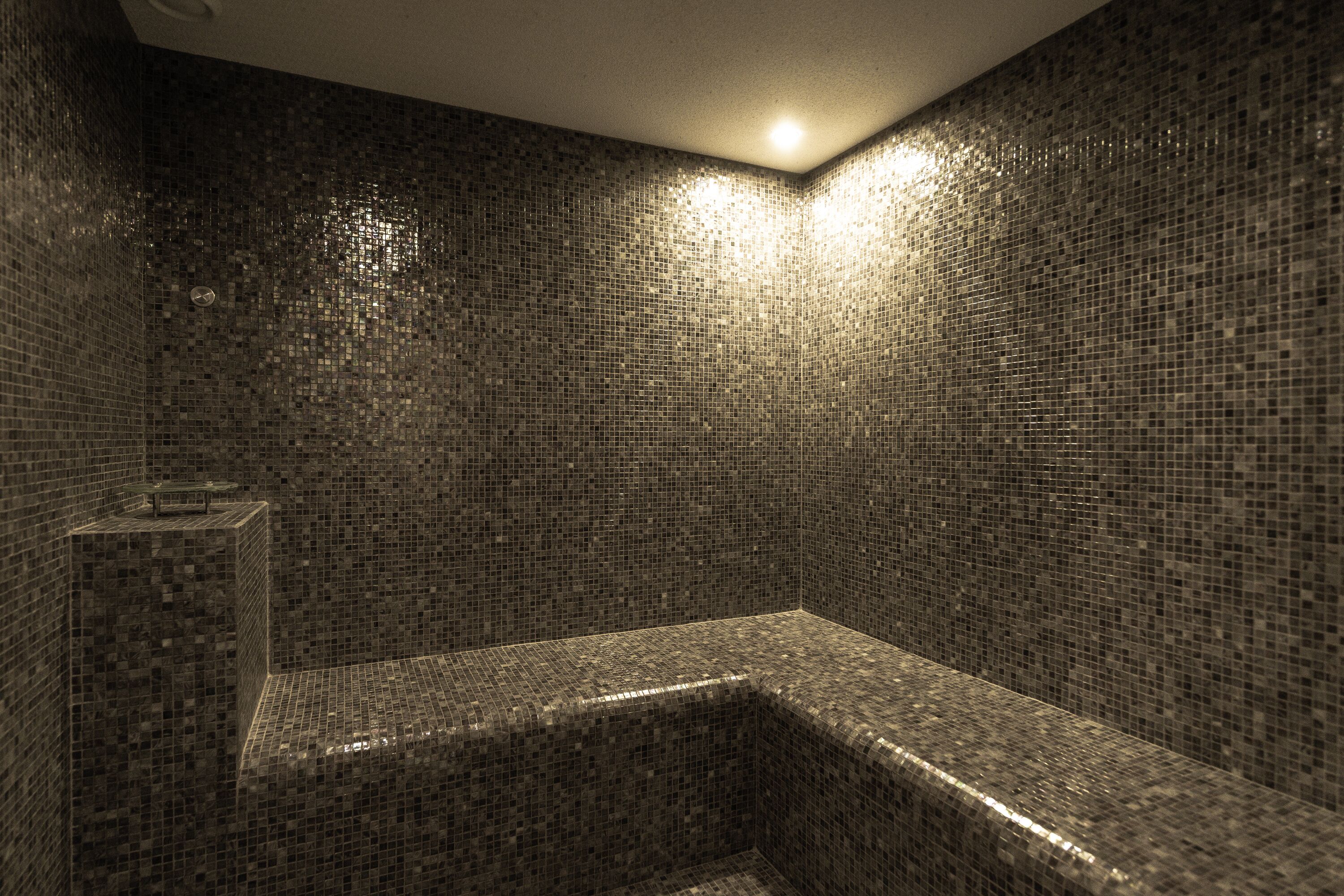 A small, enclosed shower area with mosaic tile walls and a bench.