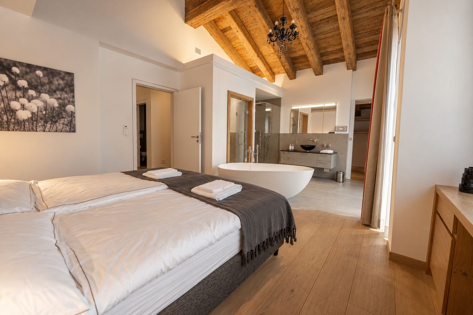 A modern bedroom with a large bed, a bathroom with a bathtub, and a wooden ceiling.