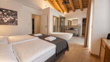 A modern bedroom with a large bed, a bathroom with a bathtub, and a wooden ceiling.