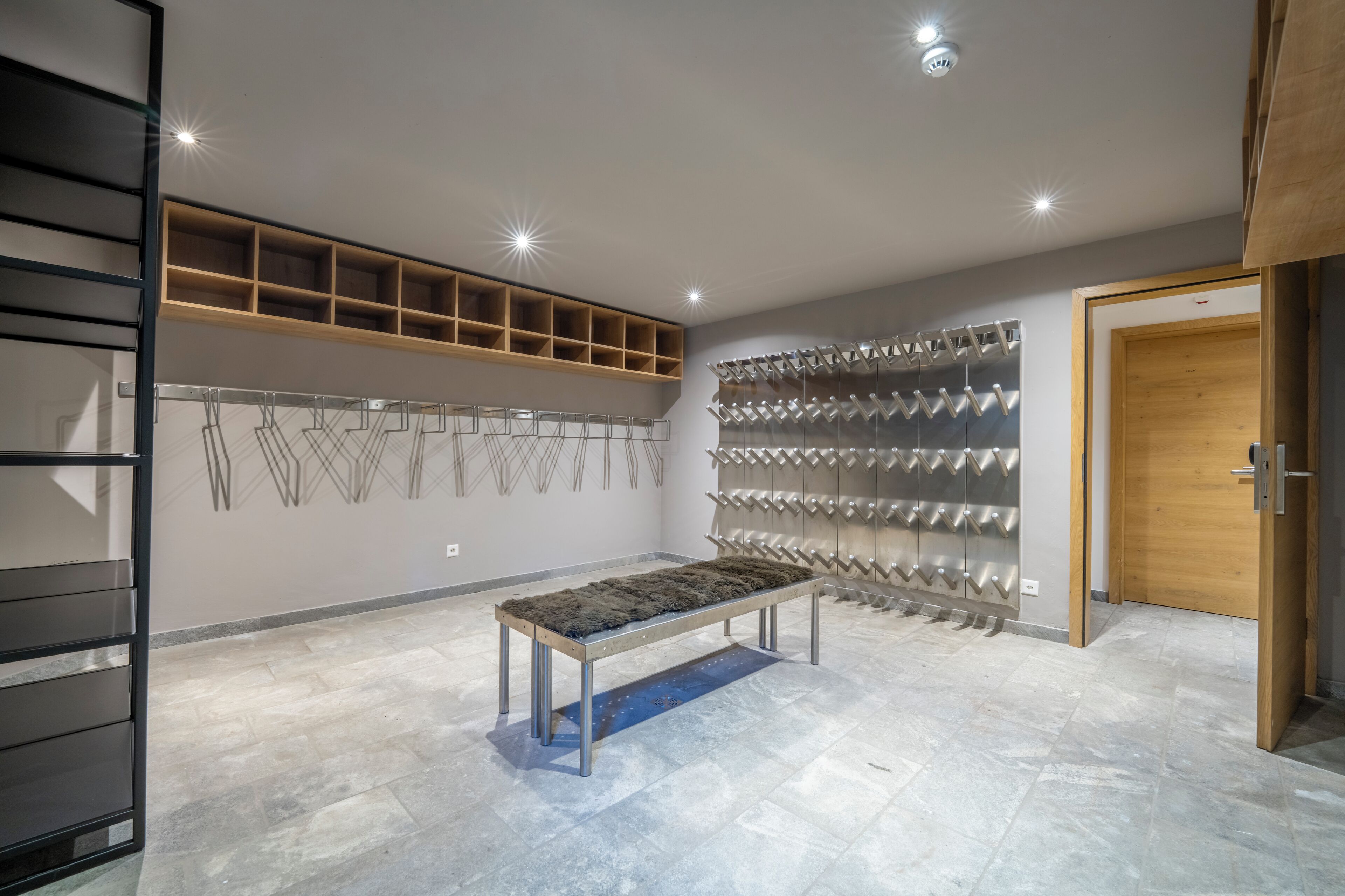 A modern interior with a bench, metal rack, wooden shelves, and a door.