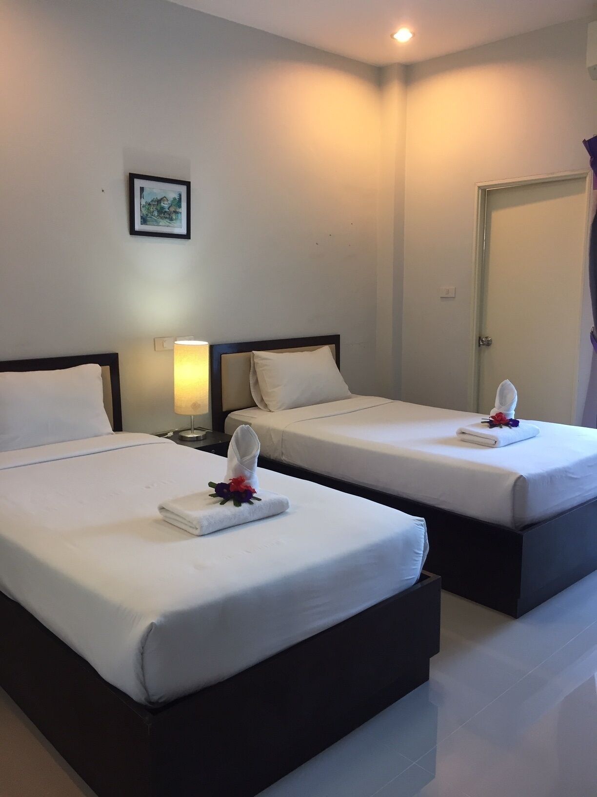 A hotel room with two beds, each with a white bedspread and pillows, a bedside lamp, and a framed picture on the wall.