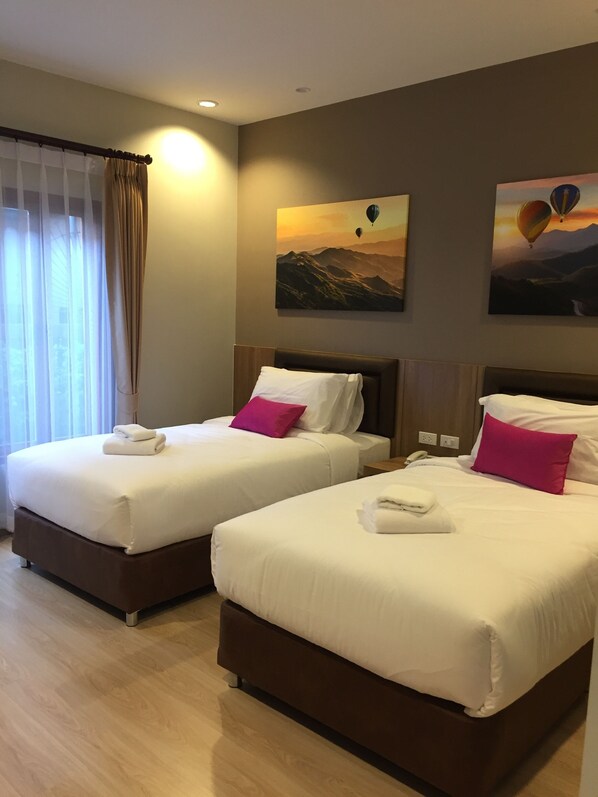A hotel room with two beds, each with white bedding and a pink pillow. There are two paintings on the wall depicting hot air balloons.