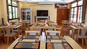 Un espace repas comprenant plusieurs tables et chaises, un téléviseur et un réfrigérateur.