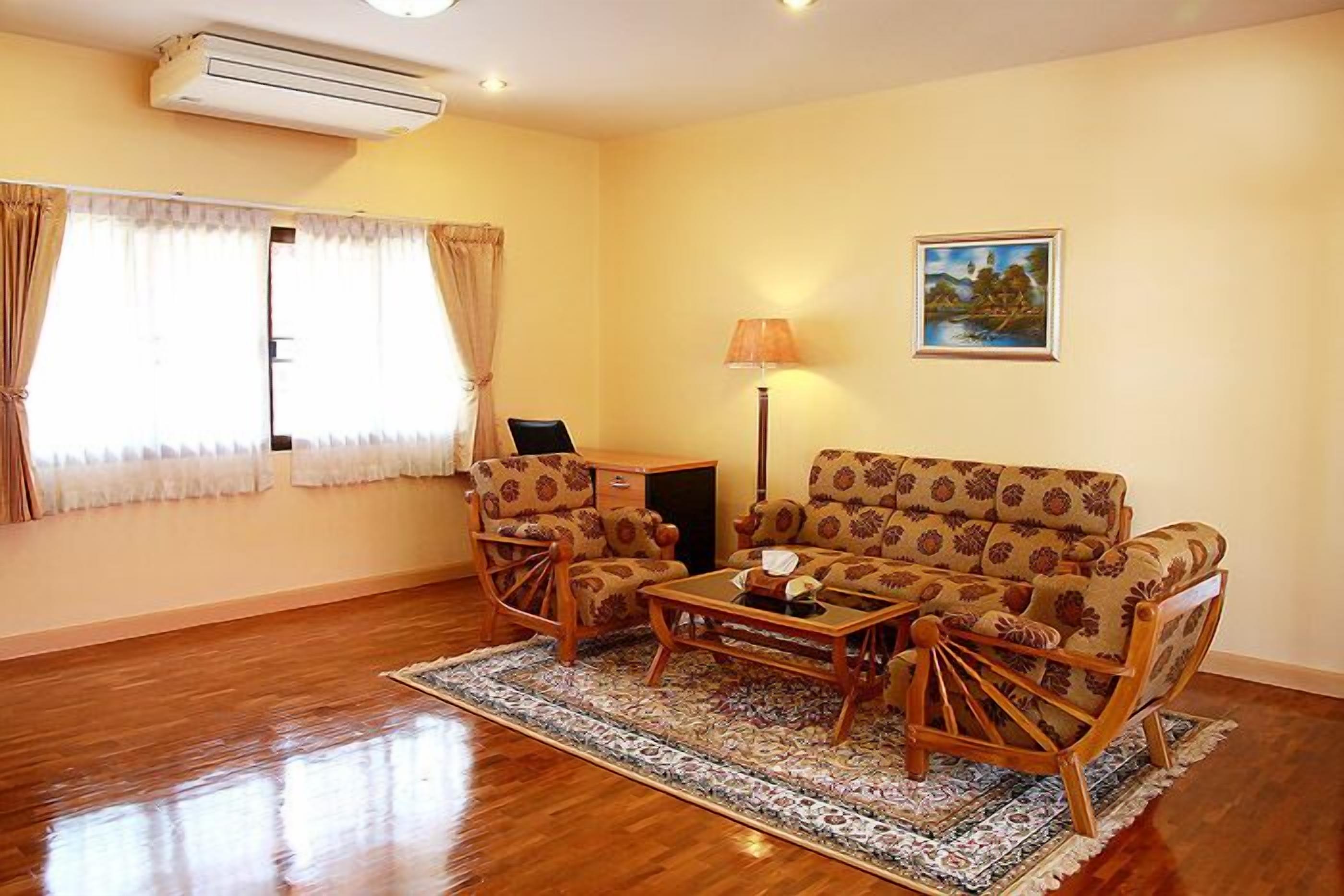 A living room with a sofa, two armchairs, a coffee table, a lamp, and a painting on the wall.