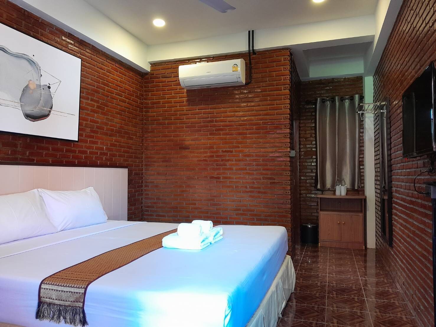 A hotel room with a large bed, a brick wall, an air conditioning unit, and a shower area.
